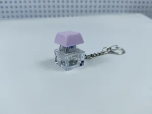 Close-up view of a transparent mechanical keyboard switch keychain with a purple keycap.