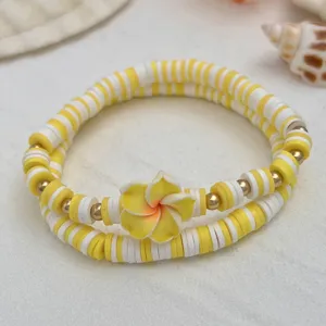 Detailansicht des gelben und weißen Heishi-Perlenarmband-Sets mit einer Frangipani-Blüte.