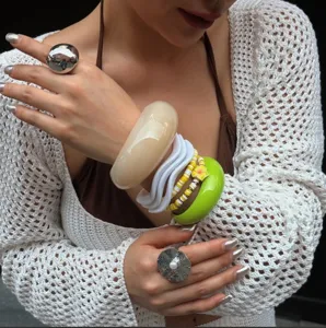 Detailansicht von gestapelten bunten Macaron-Resin-Armbändern und klobigen Silberringen