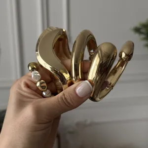 Macro shot of chunky gold-tone irregular bangles and a pearl bracelet held in hand