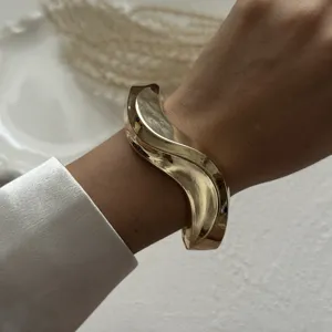 Detailed view of a stylish gold irregular wave bangle worn on a wrist with silk sleeve