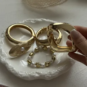 Close-up view of a hand holding stylish gold-toned alloy bangles and pearl bracelets