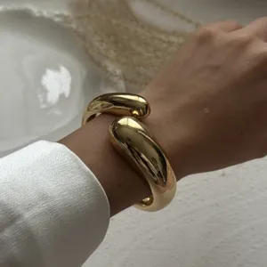 Close-up detail of a chunky gold-tone smooth waterdrop wrap bracelet on a wrist