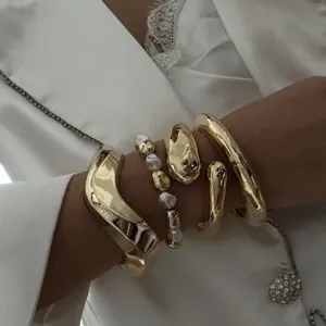 Macro detail of layered chunky gold-tone bangles and pearl bracelet set on model
