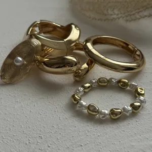 Close-up detail of gold waterdrop hug bangle and pearl ring set on textured background