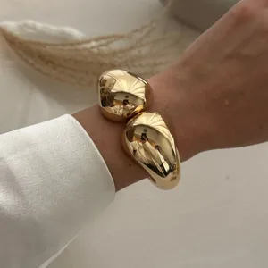 Nahaufnahme eines hochglänzenden, vergoldeten Armreifs mit doppeltem Tropfen-Design
