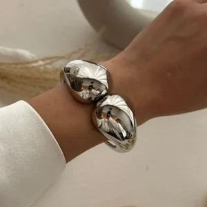 Nahaufnahme eines glänzenden silbernen ovalen Armreifs mit schwerem Doppel-Tropfen-Design