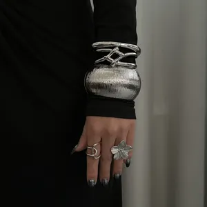 Detailaufnahme von klobigem silbernem Metallarmreif und passendem Blumenring am Modell.