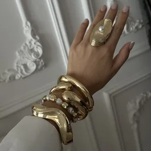 Close-up of bold gold-toned irregular bangles and a textured pearl ring on a hand