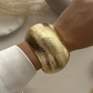 Makroansicht eines breiten, goldenen Metallarmreifs mit Textur zu einer weißen Seidenbluse.
