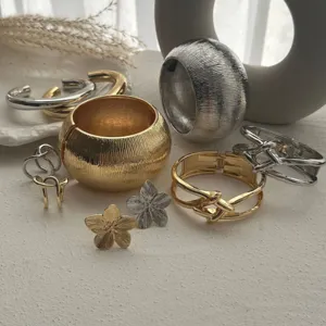 Kollektion massiver Metallarmbänder und Blumenringe in Gold- und Silbertönen