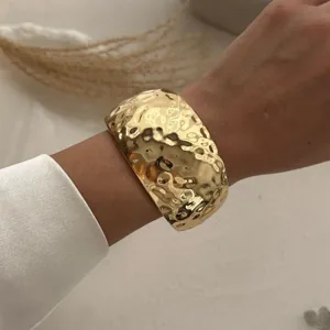 Detailaufnahme eines breiten, gehämmerten goldenen Armreifs am Handgelenk für Chic