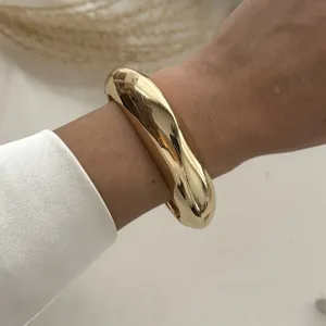 Detailansicht eines massiven goldfarbenen Armreifs im Wassertropfen-Design am Gelenk