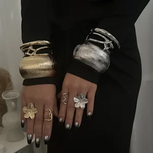 Detail von klobigen gold- und silbernen Armreifen und Blumenringen an Modelhänden.
