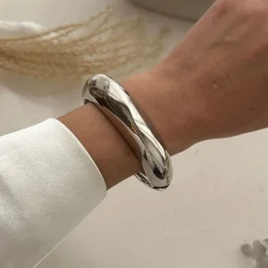 Nahaufnahme eines massiven, polierten, silberfarbenen Wassertropfen-Armreifs am Handgelenk