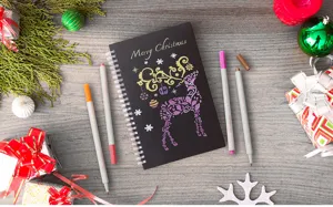 Metallische Marker-Set mit DIY Weihnachtszeichnung auf schwarzem Notizbuch
