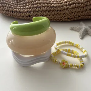 Detailansicht stapelbarer Makronen-Resin-Armreifen und gelbes Perlenarmband mit Blume