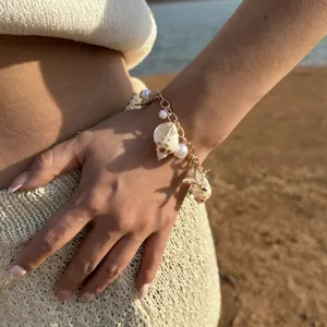 Detailed shot of a bohemian golden bracelet featuring shell, pearl and starfish charms.