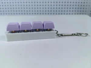 Side detail of a white mechanical keyboard keycap keychain with four purple buttons toy.