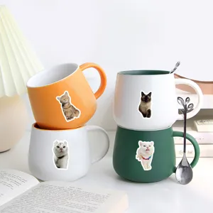 Detailed view of realistic cute cat stickers applied to colorful ceramic coffee mugs.