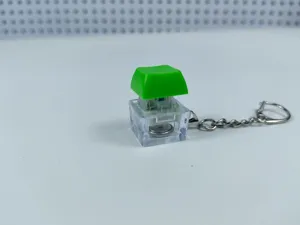 Mechanical keyboard switch keychain fidget toy with green keycap and glowing light inside.