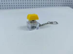 Transparent mechanical keyboard switch keychain with yellow keycap and glowing LED detail.