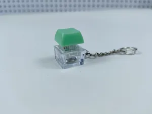 Transparent mechanical keyboard switch keychain detail, glowing fidget toy with green keycap.