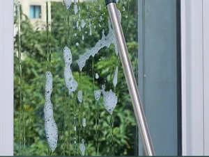 Macro detail of a durable stainless steel long-handle squeegee cleaning a soapy window