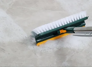 Close-up detail of a multi-functional floor scrubber brush cleaning soapy marble tiles