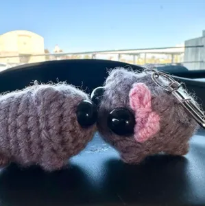 Close-up detail shot of cute crochet sad hamster keychain with big black eyes and bow.