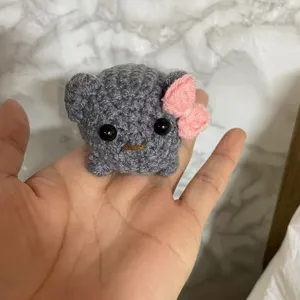 Handmade crochet sad hamster plush toy keychain, featuring cute pink bow detail in close up view.