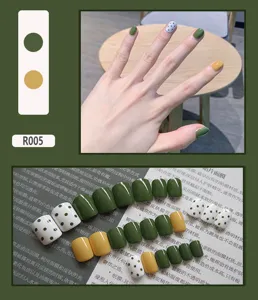 Detailed view of glossy green and yellow press-on nails with polka dot accent design