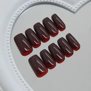 Glanzende donkerrode kunstnagels op een spiegel die dieprode tinten reflecteert.