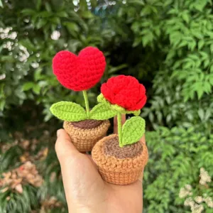 Handgemachte gehäkelte Topfpflanze Detail mit roter Herzblume und grünen Blättern.