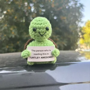 Closeup shot of a cute handmade crochet turtle holding a funny positive message sign.