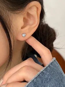 Close-up showing a delicate heart-shaped moonstone stud earring on a model's ear.