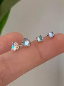 Macro view of heart and round iridescent moonstone stud earrings held on a finger