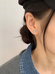 Macro view of a minimalist heart-shaped moonstone stud earring on a model's ear.