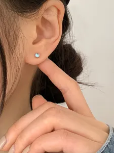 Detailed macro view of a minimalist iridescent moonstone stud earring worn on an ear