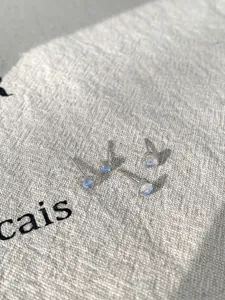 Detailed view of iridescent heart and round moonstone stud earrings on a textured linen.