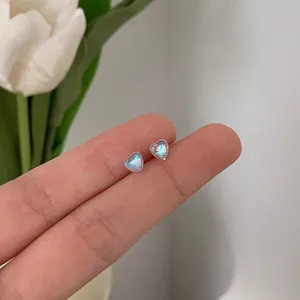 Close-up of heart-shaped moonstone stud earrings held between fingers showing size.