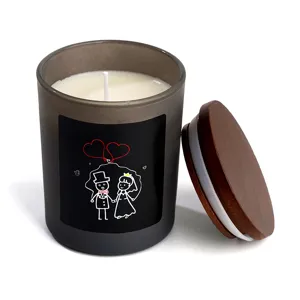 Gros plan de bougie parfumée en pot verre givré avec couvercle en bois et motif de couple.
