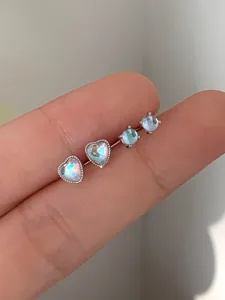 Close-up of mini heart and round iridescent moonstone stud earrings in silver settings.