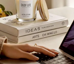 Detail view of a natural soy wax scented candle in a glass jar with wooden lid on decor books.