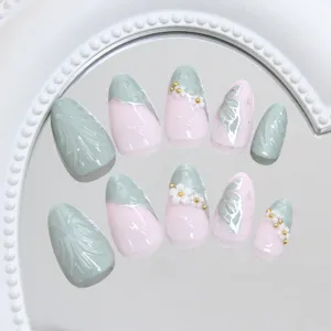 Détail de faux ongles œil-de-chat vert sauge et rose avec papillons et fleurs 3D élégantes.