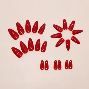 Detailed view of glossy red almond-shaped press-on nails set against cream background.
