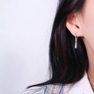 Nahaufnahme eines eleganten silbernen Wassertropfen-Ohrrings am Ohr des Models