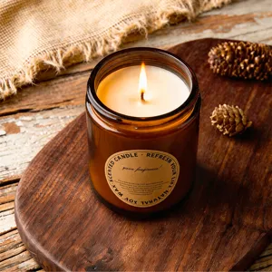 Close-up of burning scented soy candle in amber glass jar on rustic wooden board.