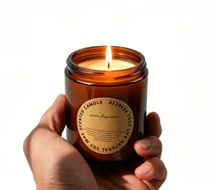 Amber glass jar scented soy candle detail view showing warm burning flame and custom label.