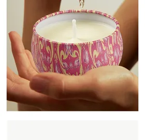 Close-up of a decorative pink and yellow patterned tin scented candle held gently in hands